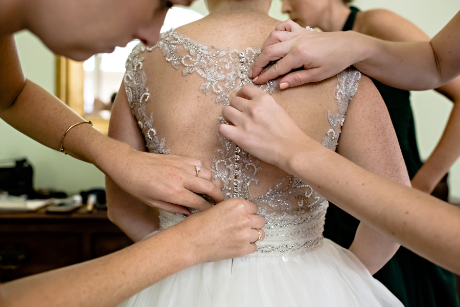Bridesmaids help button up the brides wedding dress.